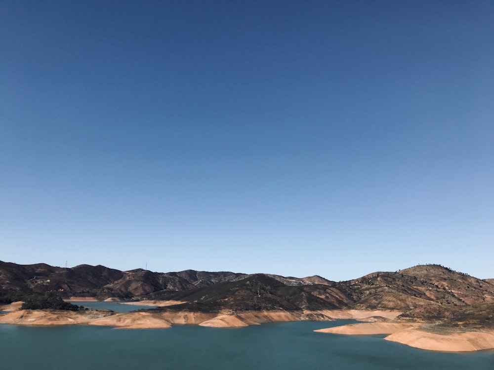 brown and white mountains beside body of water under blue sky during daytime