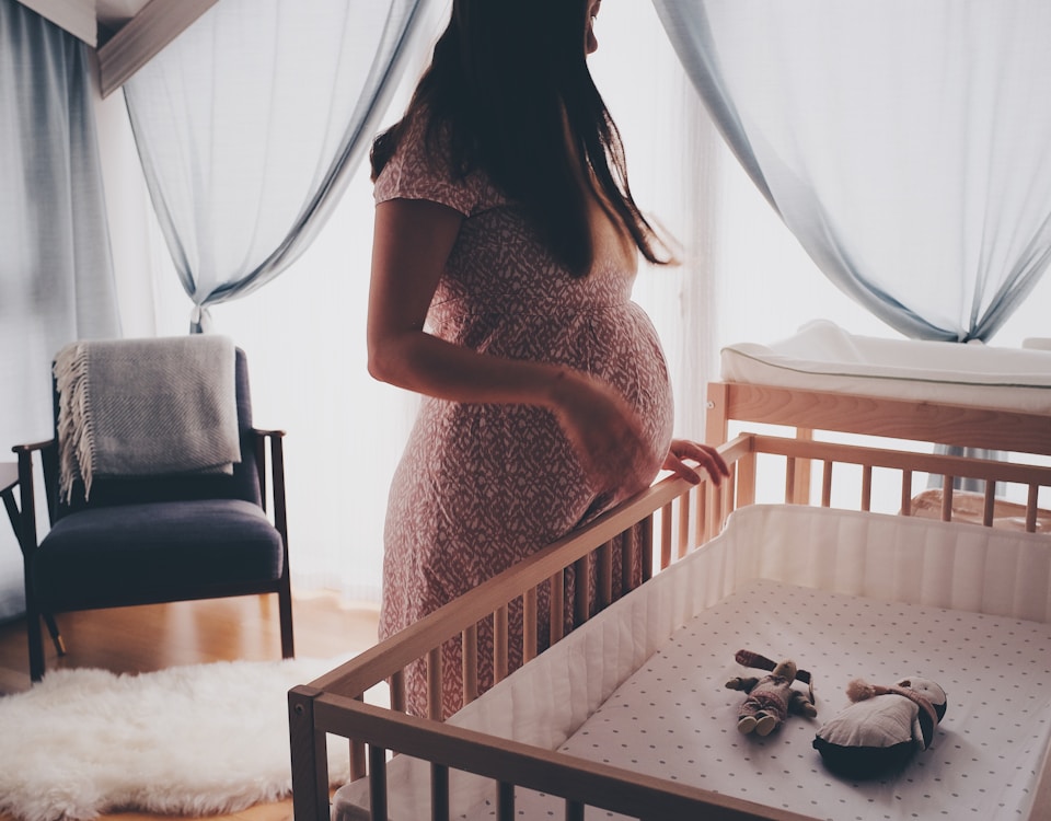 woman in white lace sleeveless dress standing beside brown wooden crib