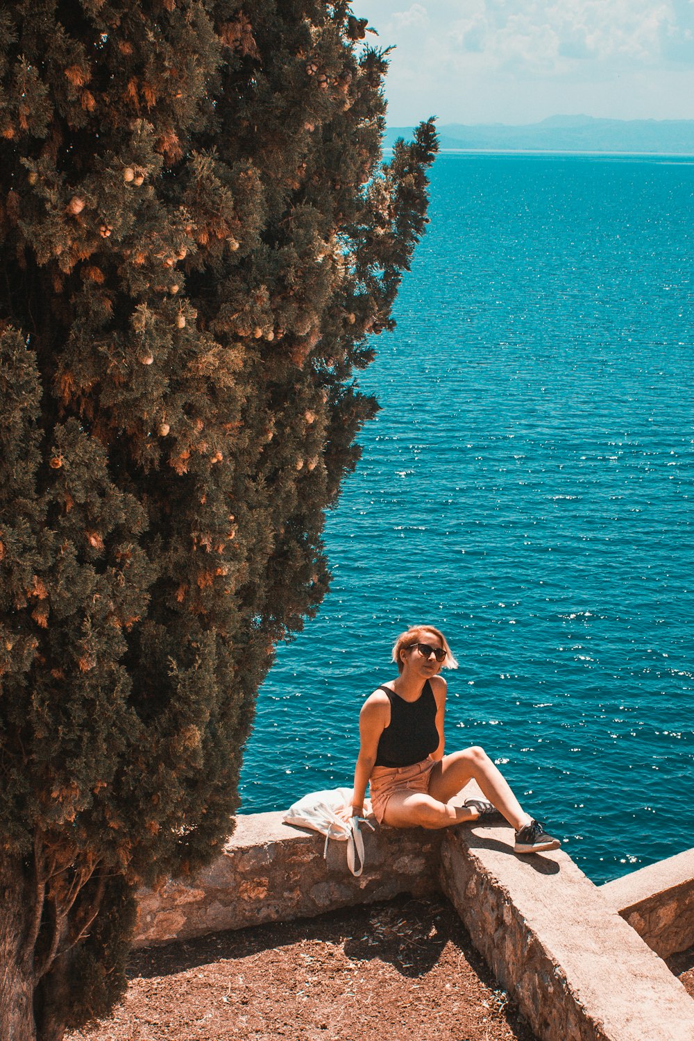 Mujer en bikini blanco sentada en la roca cerca del cuerpo de agua durante el día
