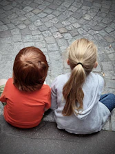 2 woman in red and gray hoodie sitting on gray concrete pavement during daytime