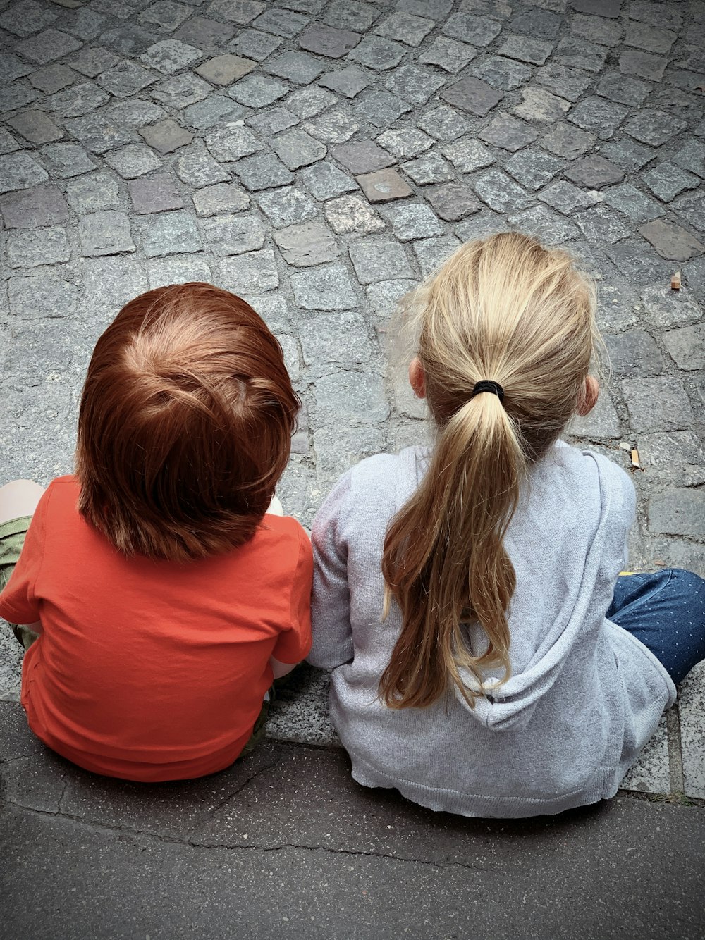 2 woman in red and gray hoodie sitting on gray concrete pavement during daytime