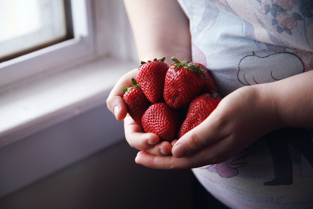 person holding red strawberries in close up photography