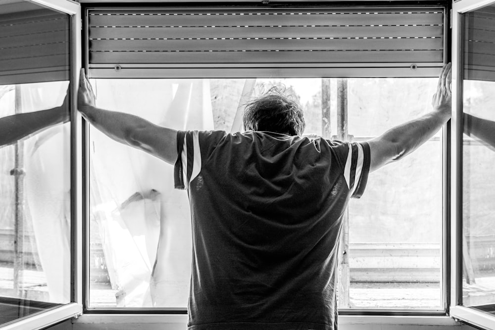 man in white t-shirt standing in front of window