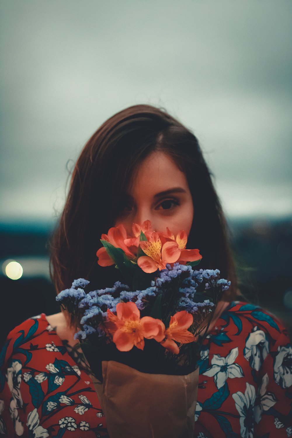 woman in red and white floral shirt holding orange flower
