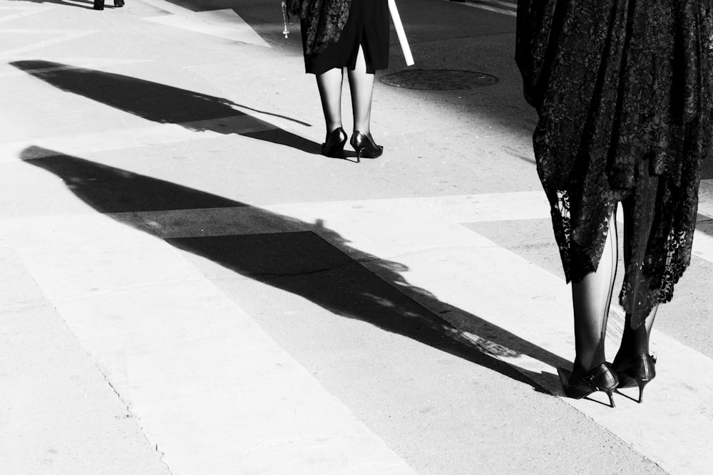 コンクリートの床に立つ黒いドレスと黒い靴の女性のグレースケール写真