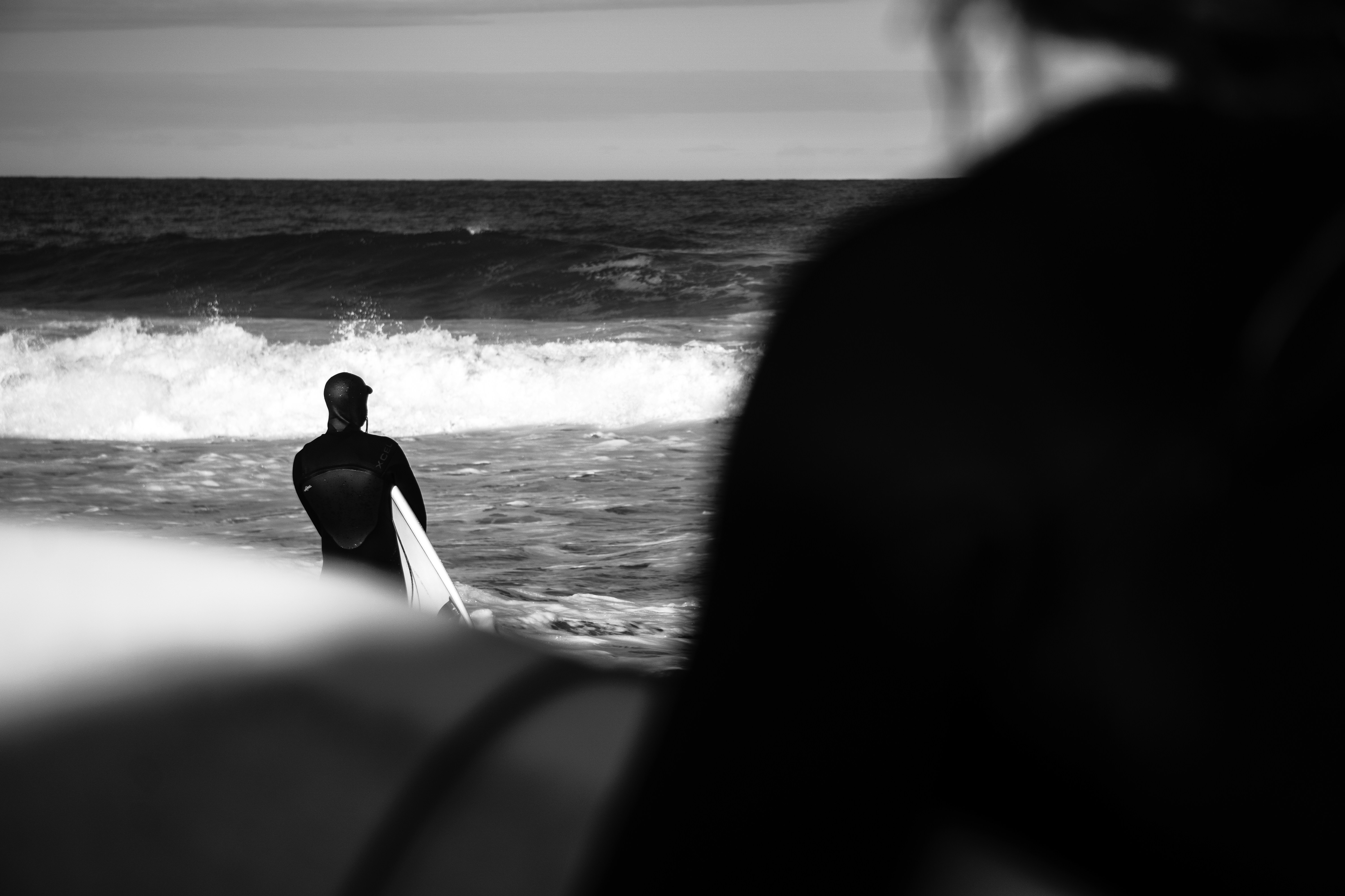 Surfer looking at the waves while another surfer walks by.