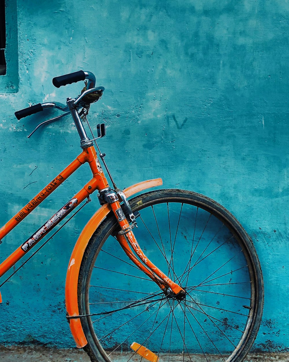 파란색으로 칠해진 벽에 기대어 있는 주황색과 검은색 자전거