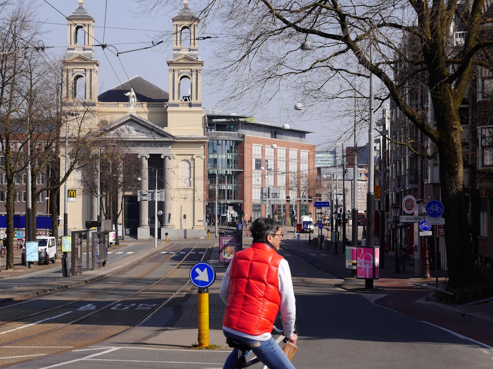 man in red jacket and blue denim jeans walking on sidewalk during daytime