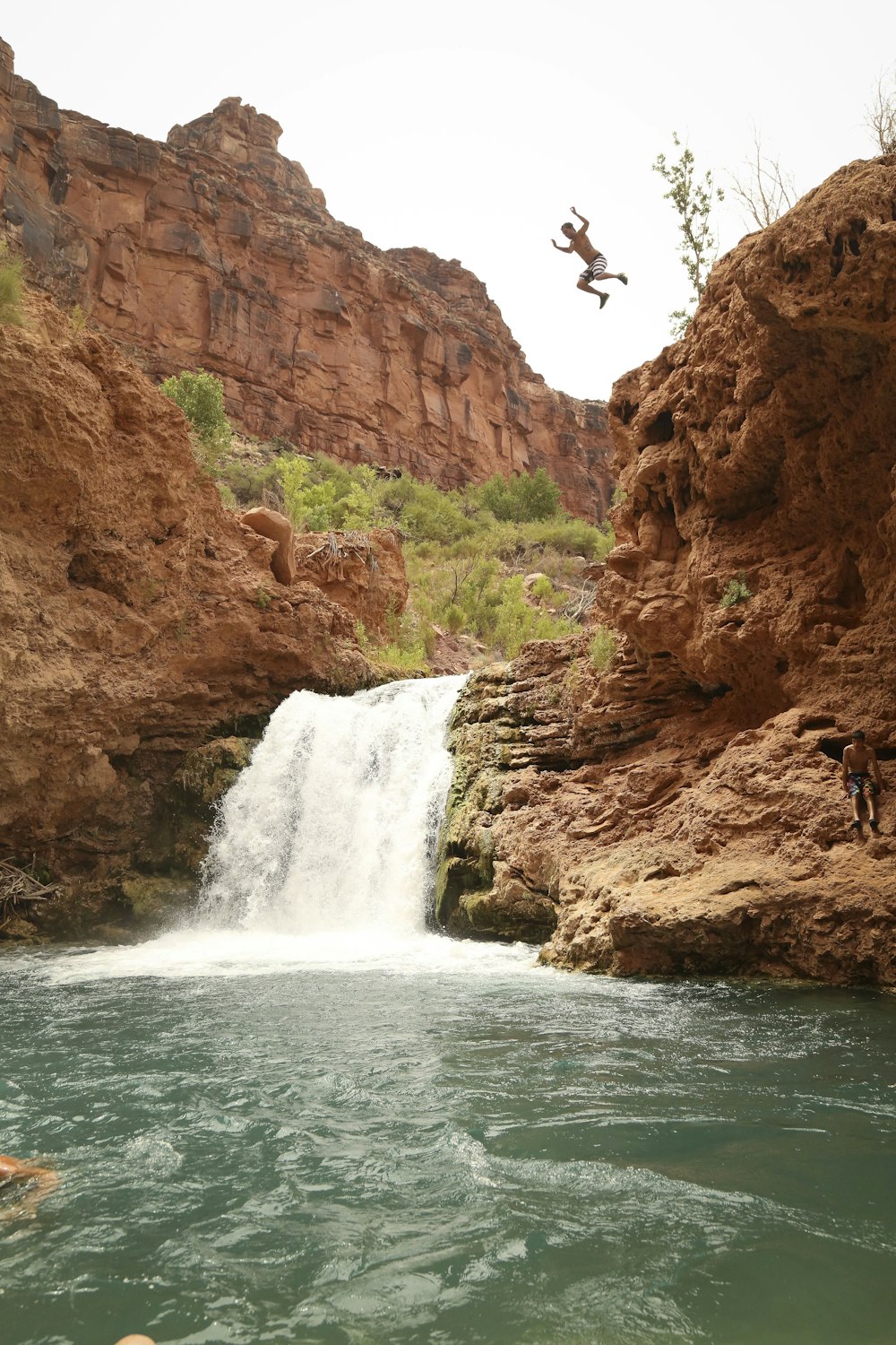 Persone in piedi sulla formazione rocciosa marrone vicino alle cascate durante il giorno