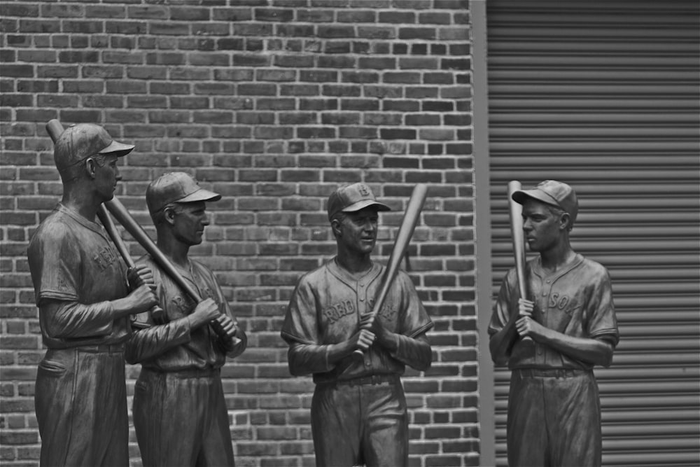 grayscale photo of 2 men standing near brick wall