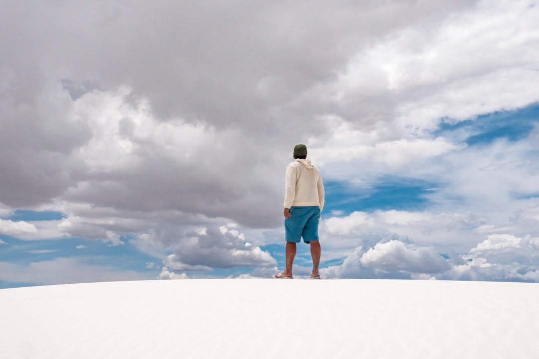 man in white hoodie and blue denim jeans standing on white clouds during daytime