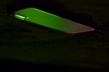A mobile phone partially illuminated with green and red lighting, creating a contrast against the dark background. The illumination highlights the phone's texture and the outline of the camera.