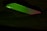 A mobile phone partially illuminated with green and red lighting, creating a contrast against the dark background. The illumination highlights the phone's texture and the outline of the camera.