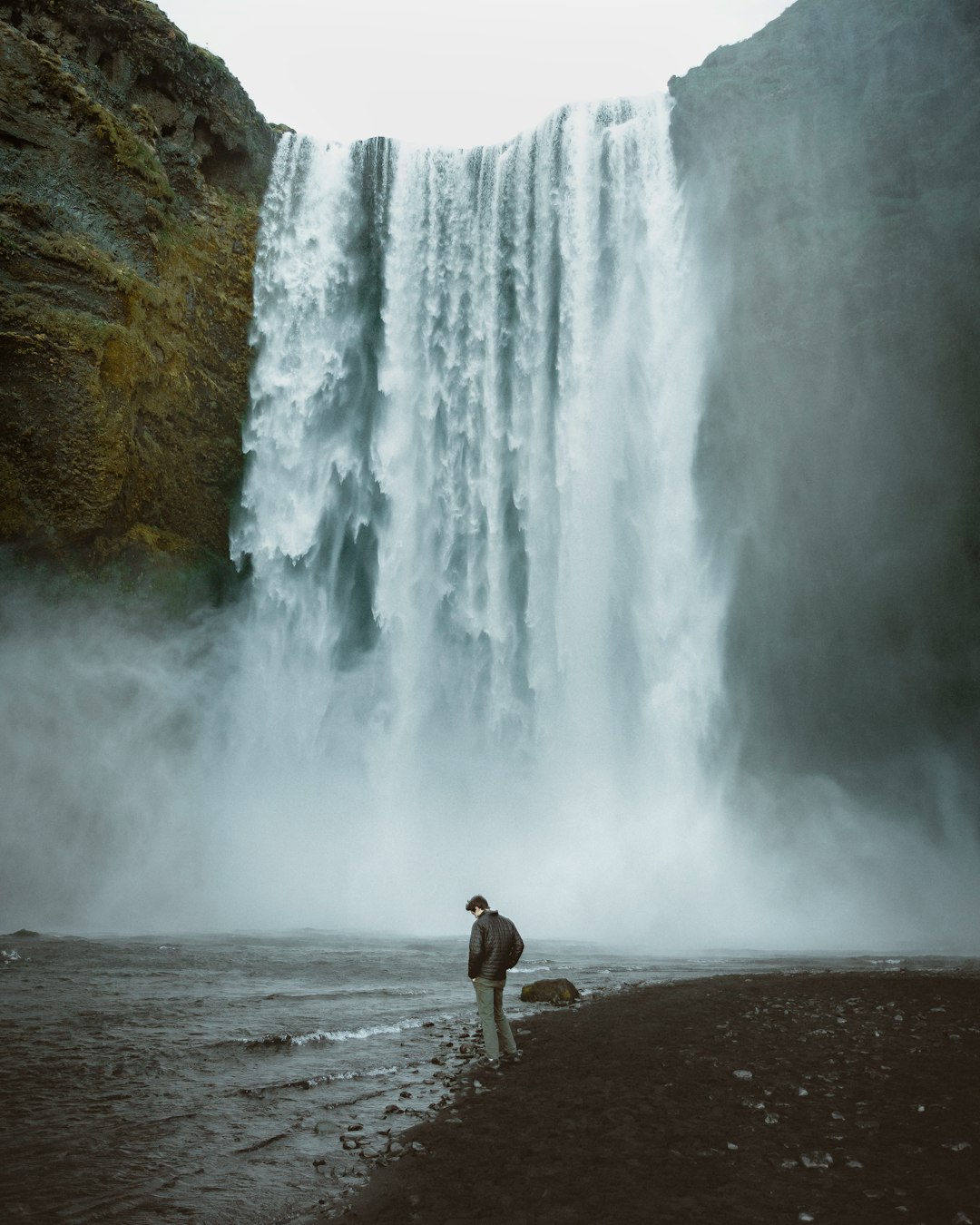 man in brown shorts standing on brown sand near waterfalls during daytime