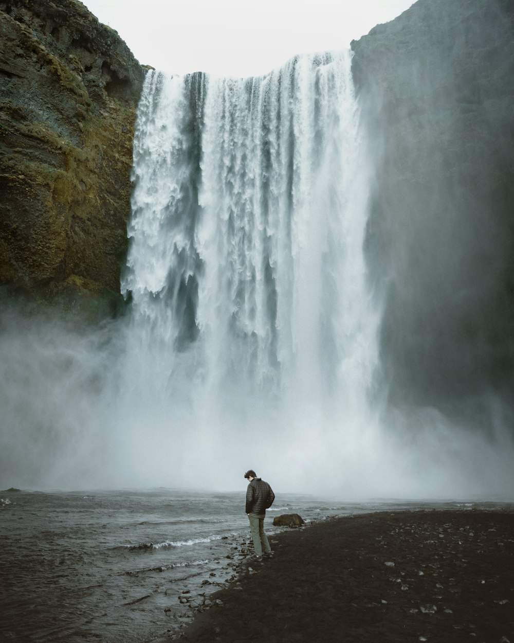 man in brown shorts standing on brown sand near waterfalls during daytime