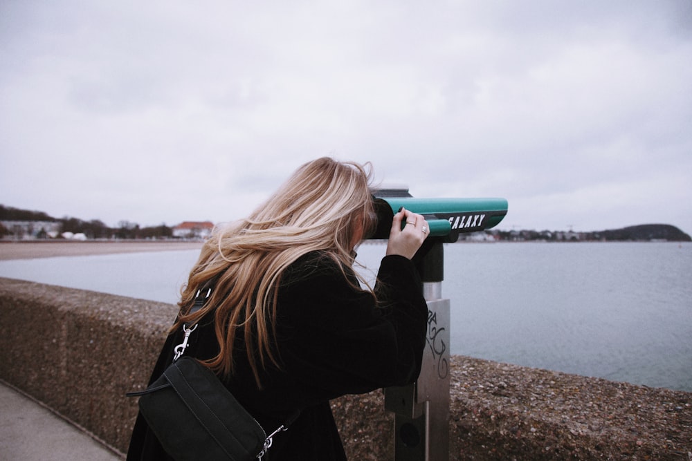 woman in black jacket holding green and white plastic cup near body of water during daytime