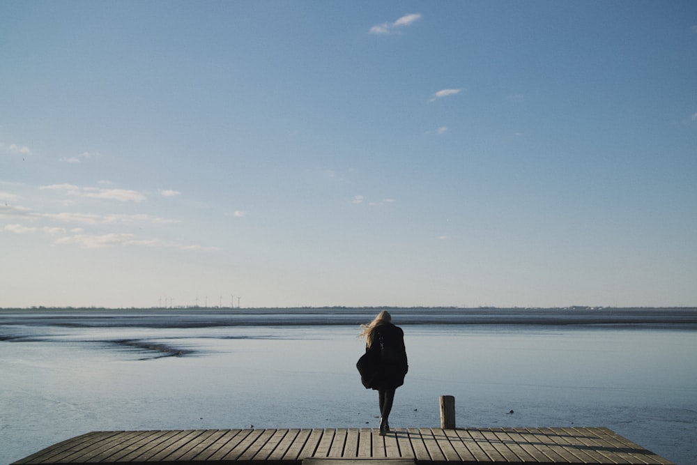 woman in black coat standing on dock during daytime