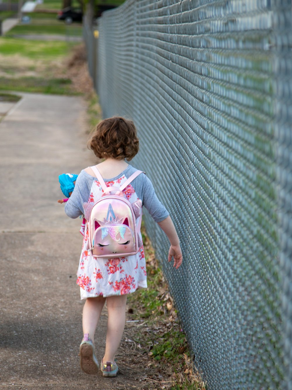 girl in white and pink floral dress standing on gray concrete pathway