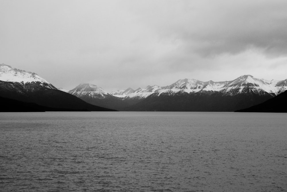 Foto en escala de grises de montañas cerca de un cuerpo de agua