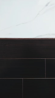 A visually contrasting surface showing white marble with subtle gray veining at the top and dark wood or tile texture below, separated by a thin border.