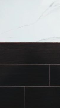 A visually contrasting surface showing white marble with subtle gray veining at the top and dark wood or tile texture below, separated by a thin border.