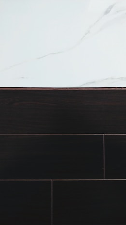A visually contrasting surface showing white marble with subtle gray veining at the top and dark wood or tile texture below, separated by a thin border.