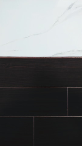 A visually contrasting surface showing white marble with subtle gray veining at the top and dark wood or tile texture below, separated by a thin border.