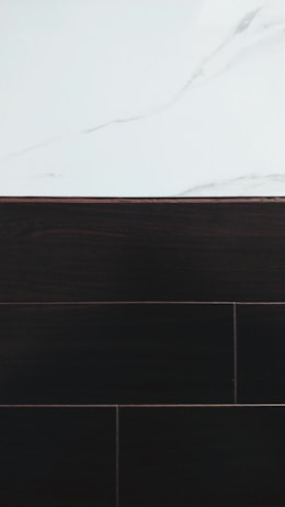A visually contrasting surface showing white marble with subtle gray veining at the top and dark wood or tile texture below, separated by a thin border.