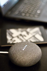 A vibrant orange smart speaker sitting on a kitchen counter surrounded by gadgets.