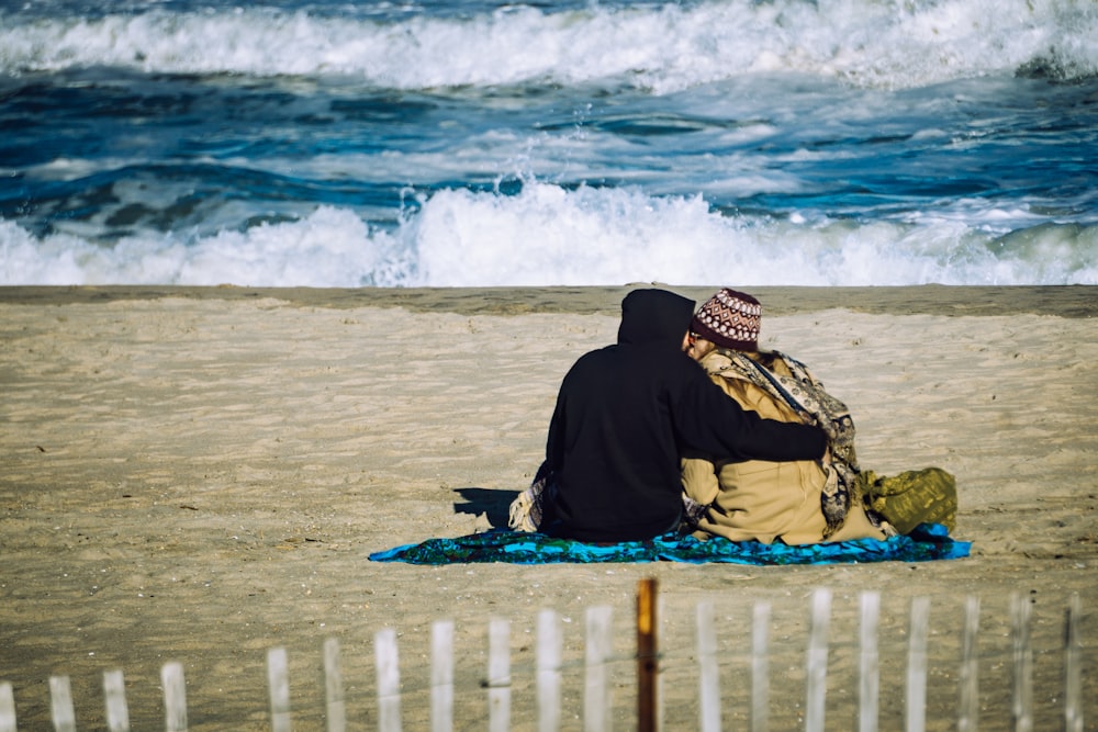 person in black hoodie sitting on beach sand during daytime