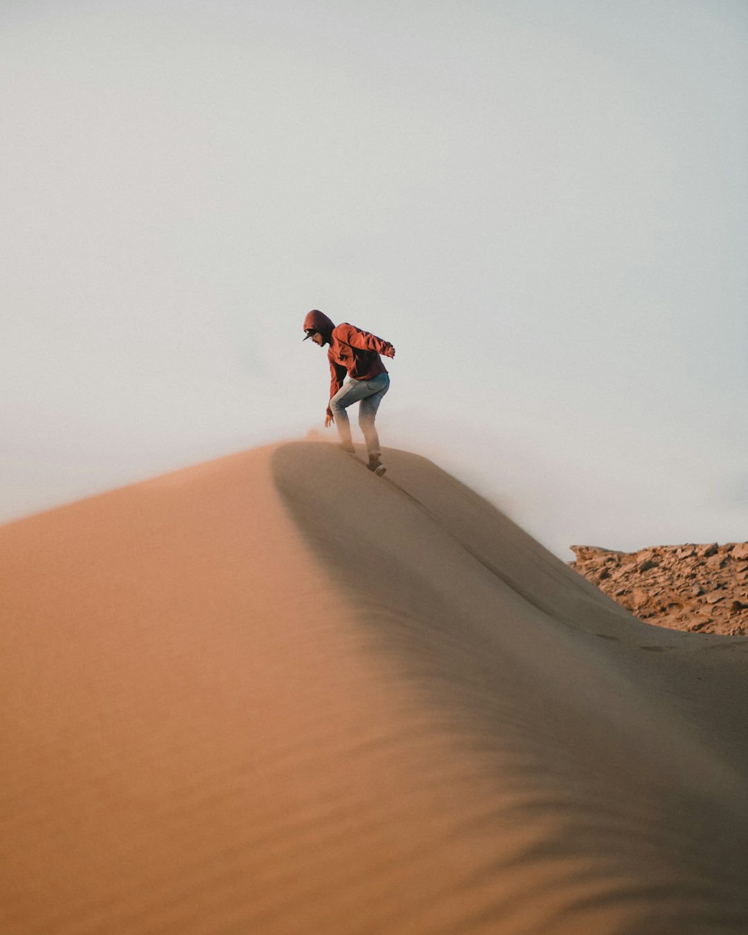 man in red jacket and white pants walking on sand dunes during daytime