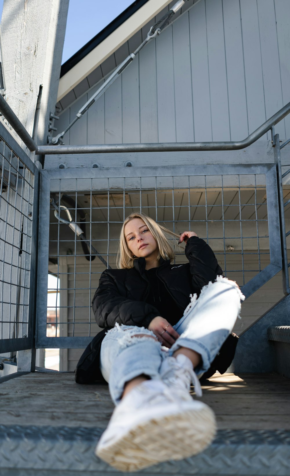 woman in black jacket and white pants sitting on white metal fence