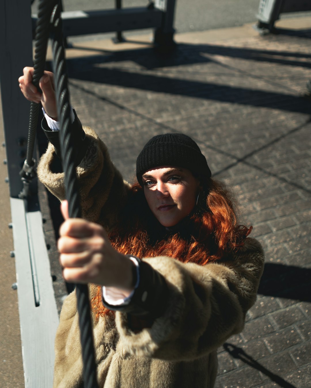 woman in black knit cap and brown fur coat holding on gray metal bar during daytime