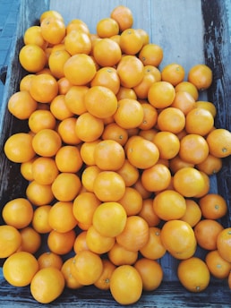 A large collection of vibrant, fresh oranges fills a rustic wooden crate. The oranges are stacked closely together, showcasing their smooth, bright surfaces.