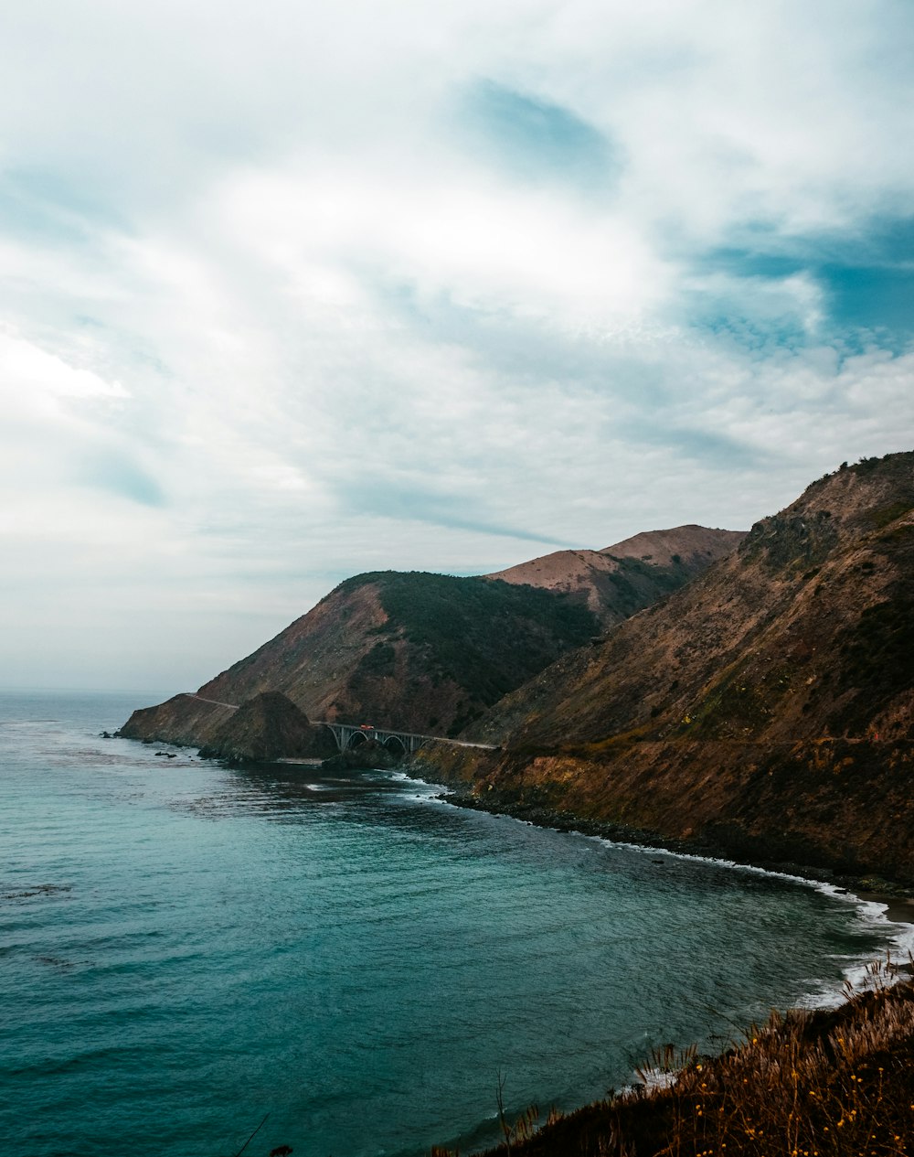 green and brown mountain beside body of water under white clouds and blue sky during daytime