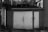 A black and white photograph of a weathered garage door, surrounded by a rough, textured wall. The scene appears old and somewhat neglected, with visible wear on the door and some overgrown grass visible on the roof.