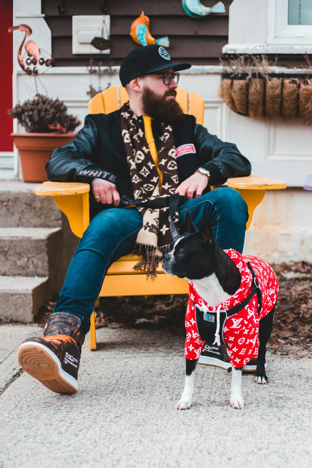 black and white short coated dog wearing red and white scarf sitting on yellow plastic chair