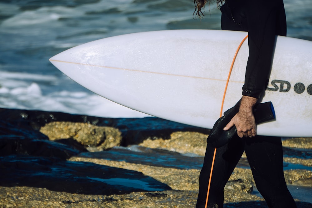 person holding white surfboard near body of water during daytime