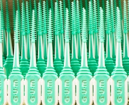 A pattern of mint green plastic dental brushes with uniform bristles lined up in rows. The design features repeated vertical elements that create a symmetrical and rhythmic appearance.