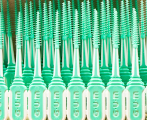 A pattern of mint green plastic dental brushes with uniform bristles lined up in rows. The design features repeated vertical elements that create a symmetrical and rhythmic appearance.