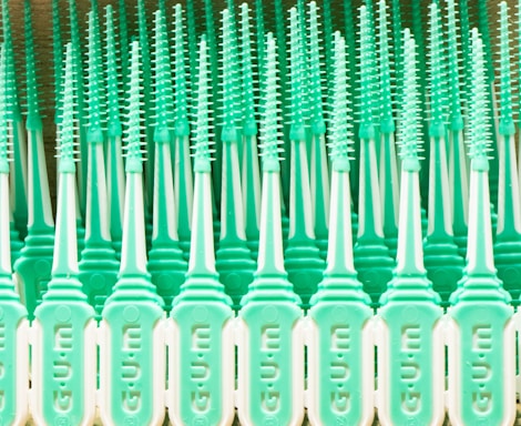 A pattern of mint green plastic dental brushes with uniform bristles lined up in rows. The design features repeated vertical elements that create a symmetrical and rhythmic appearance.