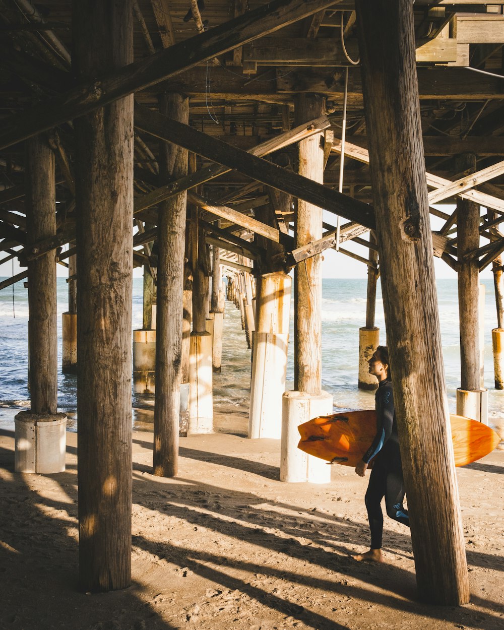 man in black jacket holding brown surfboard walking on beach during daytime