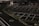 A dimly lit empty parking lot with marked parking spaces including numbered spots and painted arrows. There is a security booth at one end, surrounded by traffic cones and a gate mechanism. The area is fenced in and appears to have been photographed at night.