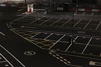 A well-lit parking area with clearly marked spaces and a security guard checking the entrance.