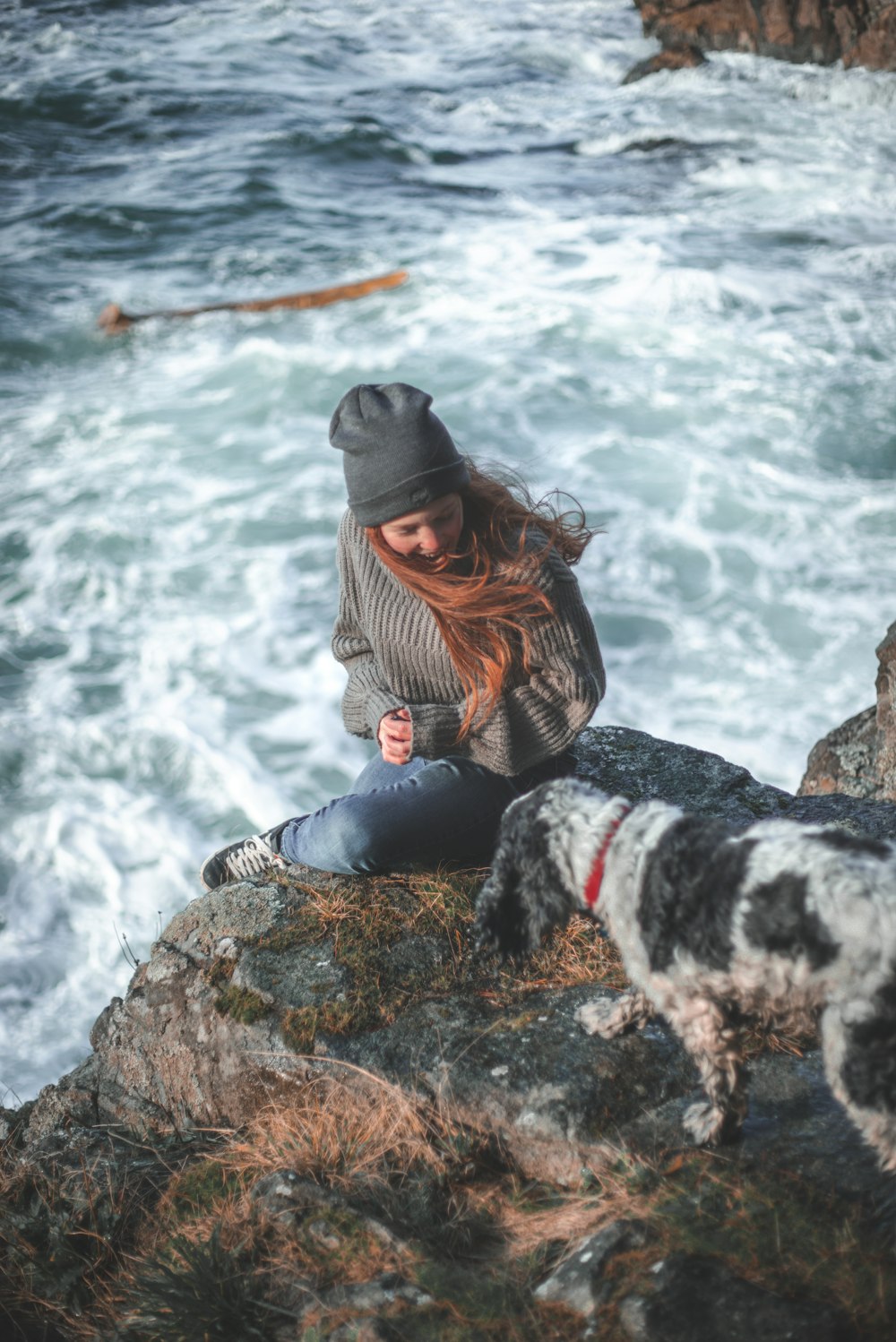 woman in gray sweater and black pants sitting on rock by the sea during daytime