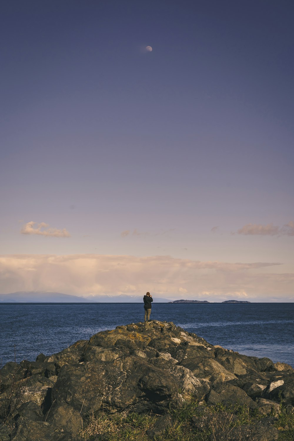 person standing on rock formation near sea under blue sky during daytime