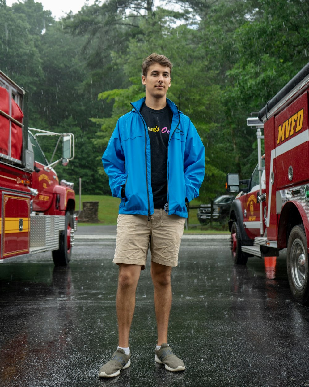 man in blue zip up jacket and brown shorts standing on wet road during daytime