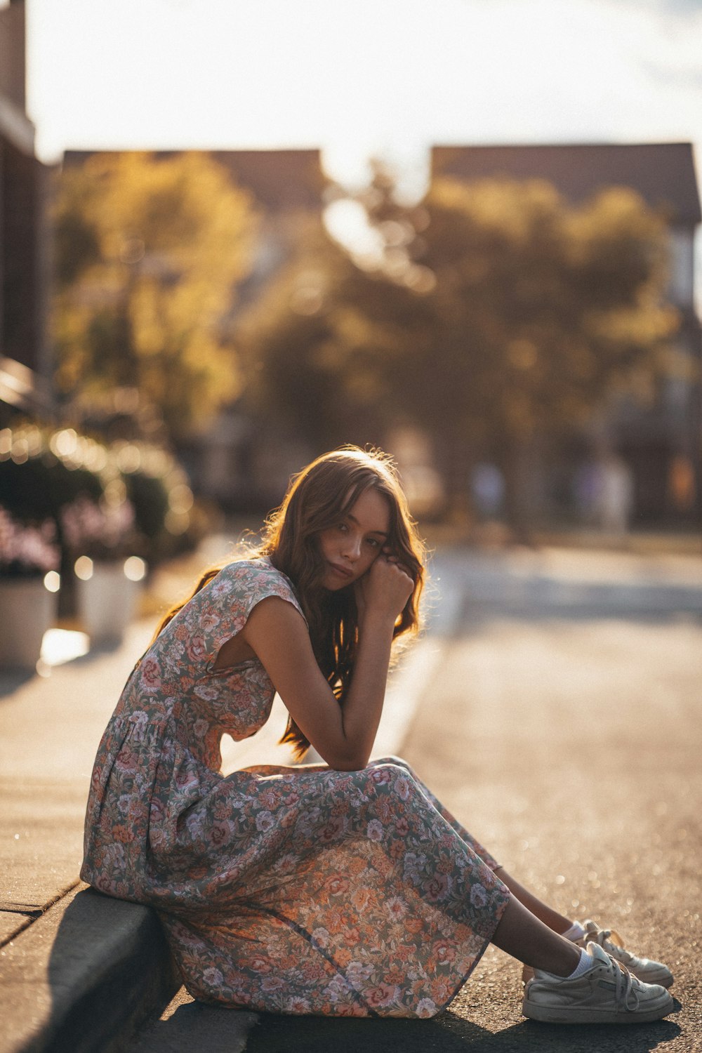 woman in white and brown floral dress sitting on gray concrete road during daytime