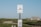 A clear blue sky over a bus stop sign for Martha's Vineyard Transit Authority is visible. The sign is mounted on a wooden post with a schedule attached below. In the background, there is a small house and green shrubbery set in a landscape that appears rural.