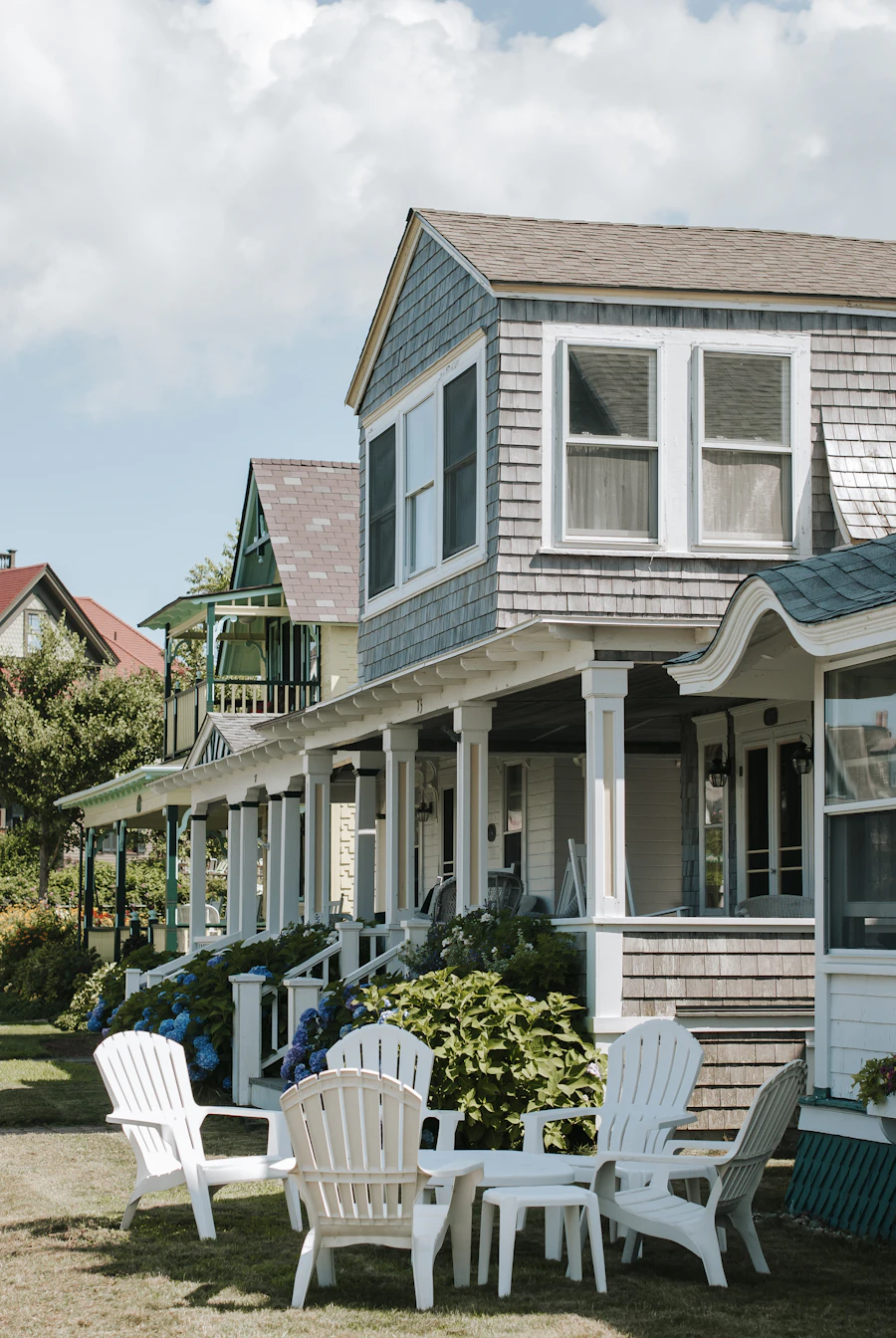 Shingled cottage with a deep porch and white Adirondack chairs on the lawn